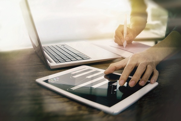 Person schreibt an Laptop und Tablet